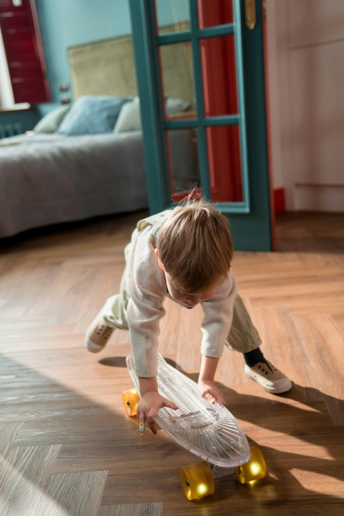 Kiddo playing with his skateboard on the floor with sunlight on his back